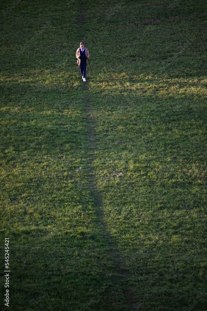 Lady walks downhill nordic walking on a meadow Lady walks downhill nordic walking on a meadow