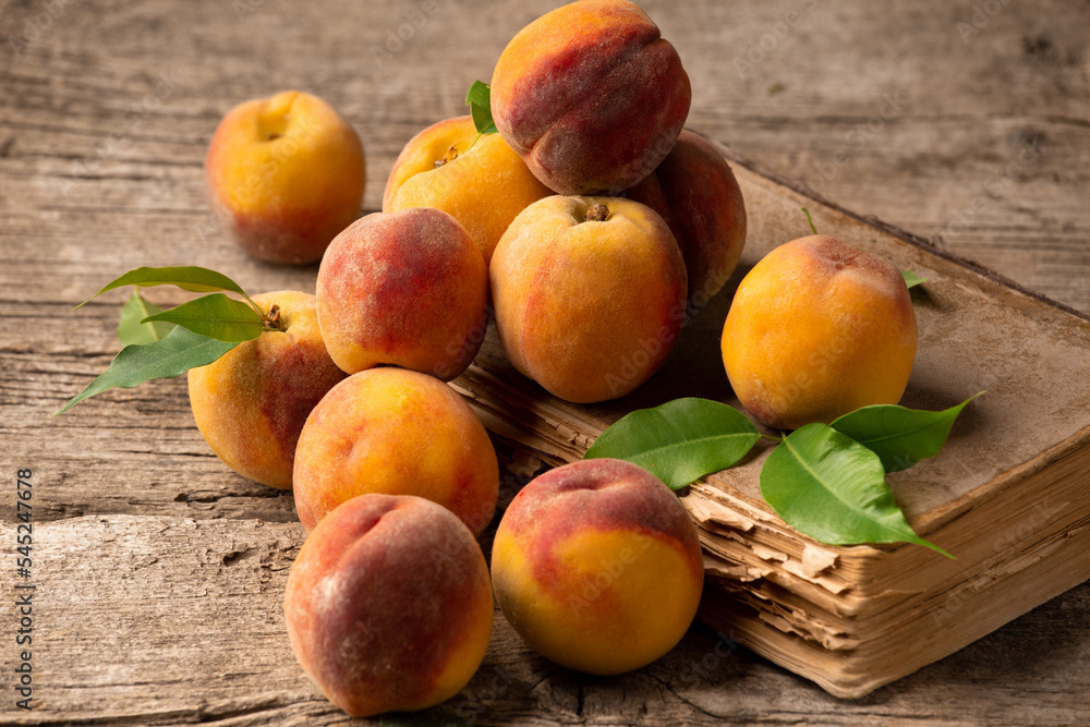 Peaches with green leaves lie on a book and a wooden background. Peaches with green leaves lie on a book and a wooden background.