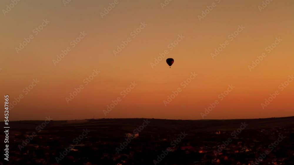 Aerial of a silhouette of an air balloon flying against the golden sunset sky over the countryside Aerial of a silhouette of an air balloon flying against the golden sunset sky over the countryside
