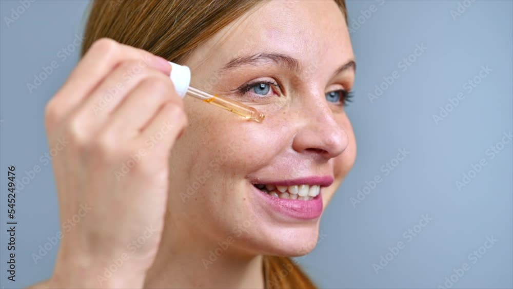 A young caucasian smiling woman is applying a cosmetic oil to her face. Slow motion A young caucasian smiling woman is applying a cosmetic oil to her face. Slow motion