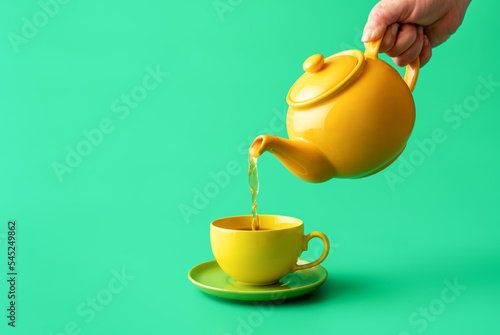 Pouring tea from a teapot in a cup, isolated on a green background