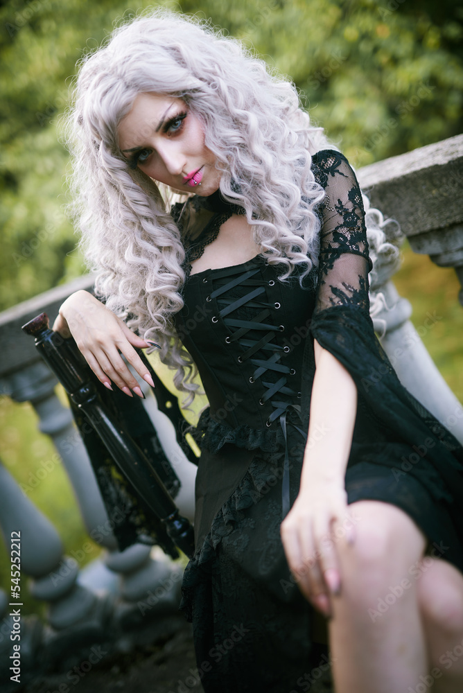 Portrait of a gothic girl, looking like a doll lolita, posing next to an old stone staircase of a castle or an old abandoned tower