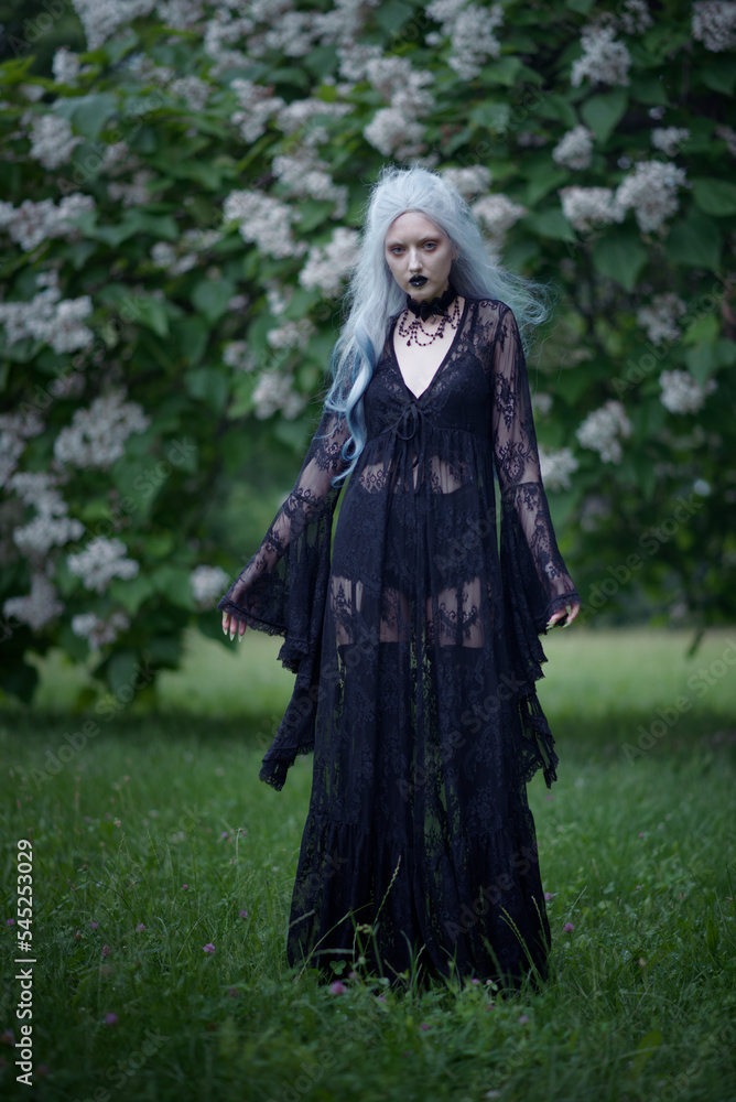 Dark goth girl standing in the forest, portrait of a wiccan witch performing magic