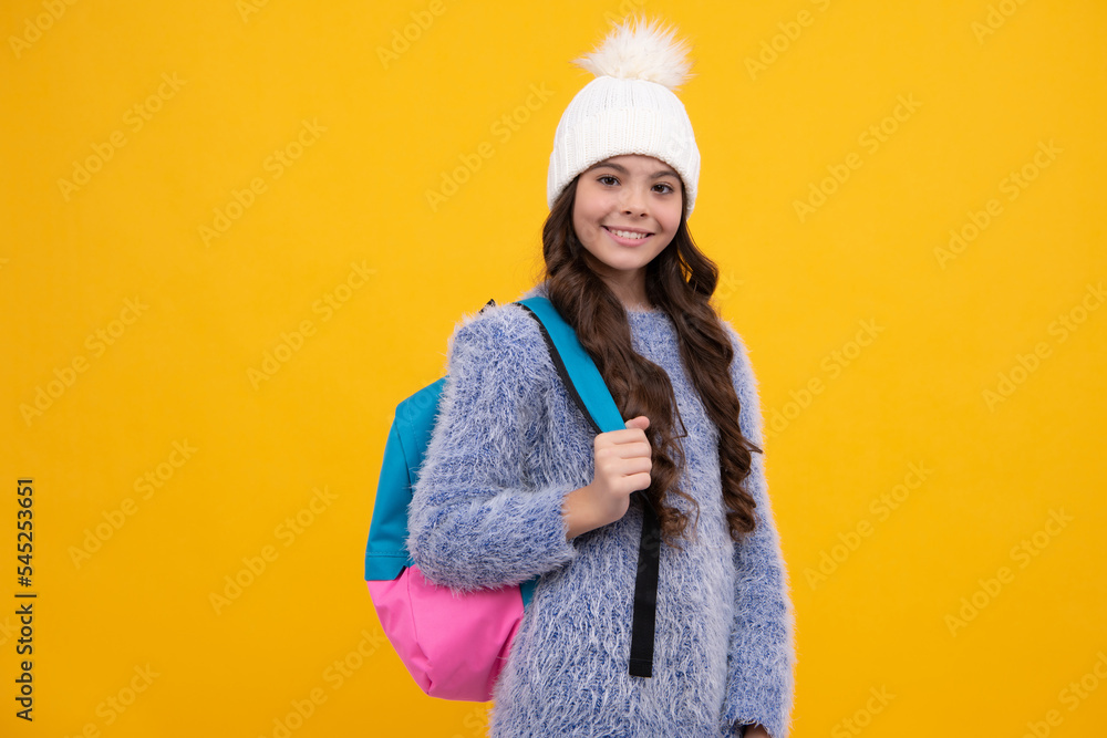 Portrait of school teenage girls in winter hat holding copybooks and backpack over yellow background. Winter school. Happy girl face, positive and smiling emotions. Portrait of school teenage girls in winter hat holding copybooks and backpack over yellow background. Winter school. Happy girl face, positive and smiling emotions.