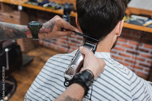 brunette man near tattooed hairdresser trimming his neck with electric hair clipper.