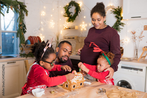 African American family decorating a gingerbread house together on Christmas day. Christmas moments with kids at home concept