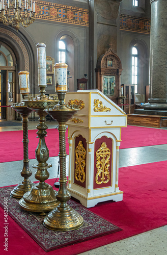 Helsinki, Finland - July 20, 2022: Uspenski Cathedral. White-golden lecture stand with 3 massive candle stands on red carpet and western wall in back photo