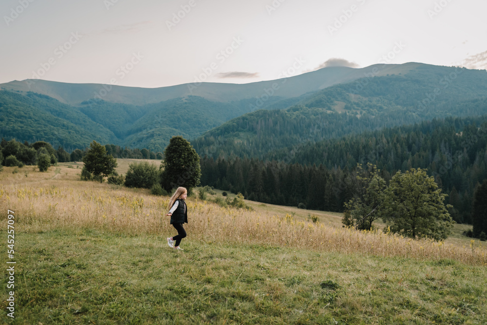 Little hiker girl running on grass in autumn mountains. Travel concept. Holiday, trip and vacation. World Tourism Day. Enjoying time kid walk on sunset on top of foggy mountain. Active outdoor games.