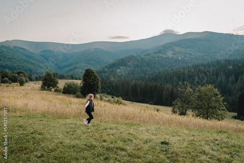 Little hiker girl running on grass in autumn mountains. Travel concept. Holiday, trip and vacation. World Tourism Day. Enjoying time kid walk on sunset on top of foggy mountain. Active outdoor games. © Serhii