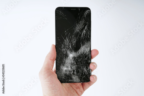 A man holds a smartphone in his hand with a broken screen on a white background