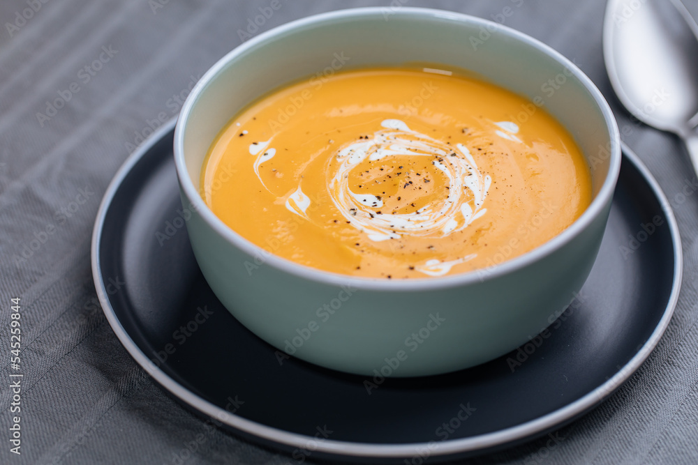 Creamy pumpkin soup garnished with cooking sauce served in turquoise dish with slice of bread in rustic mood. Seasonal warm food. Autumn Appetiser Creamy pumpkin soup garnished with cooking sauce served in turquoise dish with slice of bread in rustic mood. Seasonal warm food. Autumn Appetiser