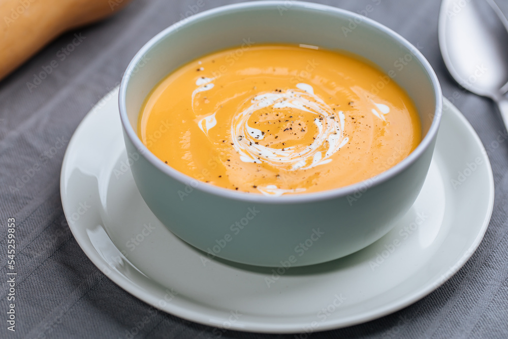 Creamy pumpkin soup garnished with cooking sauce served in turquoise dish with slice of bread in rustic mood. Seasonal warm food. Autumn Appetiser Creamy pumpkin soup garnished with cooking sauce served in turquoise dish with slice of bread in rustic mood. Seasonal warm food. Autumn Appetiser