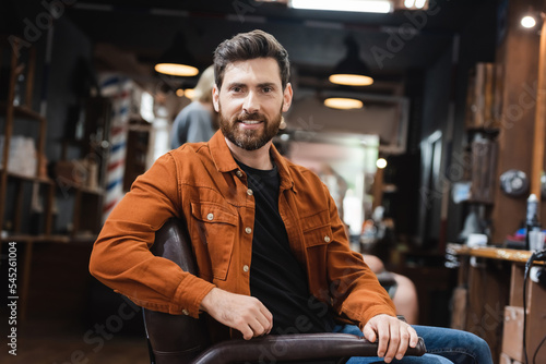 brunette bearded man sitting in beauty salon and smiling at camera.