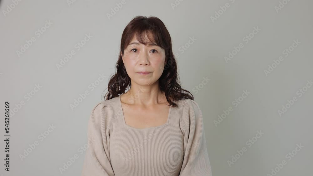 Middle aged asian woman stand still and stars the camera. White wall. Bust-up Middle aged asian woman stand still and stars the camera. White wall. Bust-up