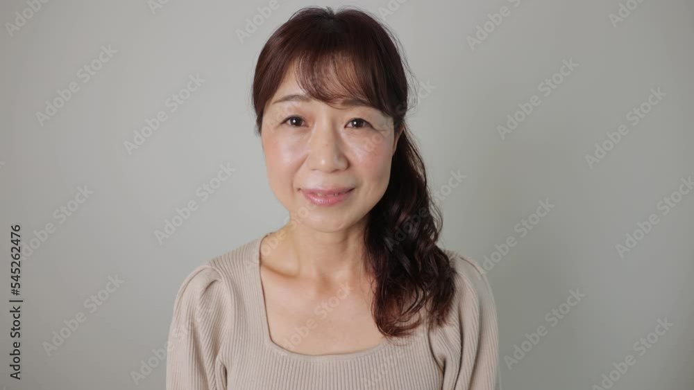 Asian middle aged woman smiles at the camera. Dolly in. White background. Asian middle aged woman smiles at the camera. Dolly in. White background.