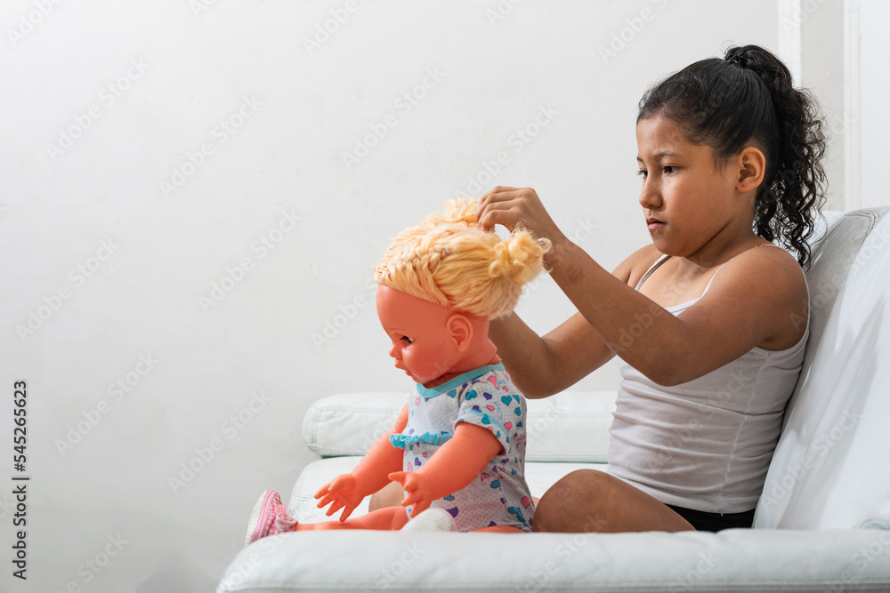 brunette girl very concentrated playing with her doll sitting on the living room sofa, latina girl playing at being a mommy. brunette girl very concentrated playing with her doll sitting on the living room sofa, latina girl playing at being a mommy.