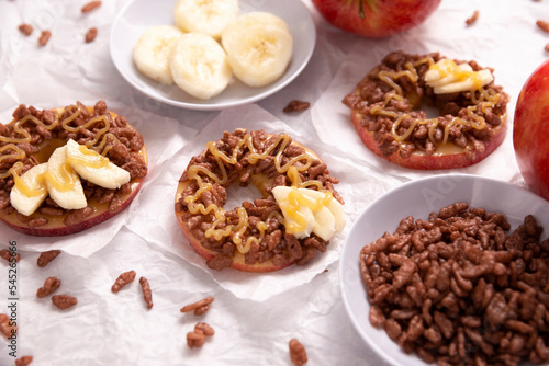 Creative party snack for holidays. Apple rounds with peanut butter  caramel and chocolate flavor puffed rice topping with banana slices. Funny appetizer for kids and adults.