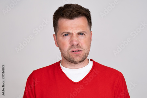 Confused guy wearing red tshirt waiting news looking at camera with doubt.