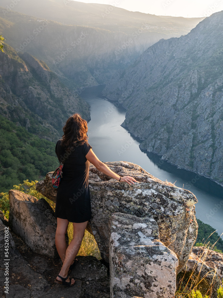 Naklejka premium Mujer de pie observando el rio desde un mirador al atardecer o el amanecer