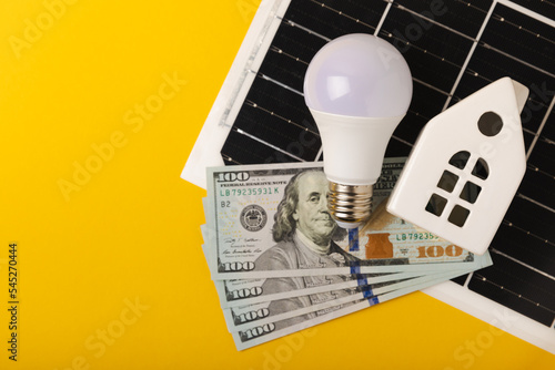 Flat lay composition with solar panel, led lamp, house model and money on  table. Money saving and clean energy concept. Ecology and sustainable development concept. photo