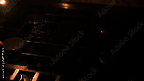 A man's hand with a match lights a gas burner or a gas stove in the kitchen. Man burn his fingers trying to burn the gas stove in the dark