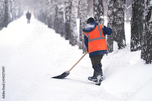 City service. A municipal worker removes snow from a pedestrian path with a shovel after a snowfall.