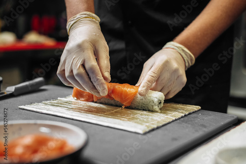 Closeup of chef hands in gloves preparing sushi rolls.