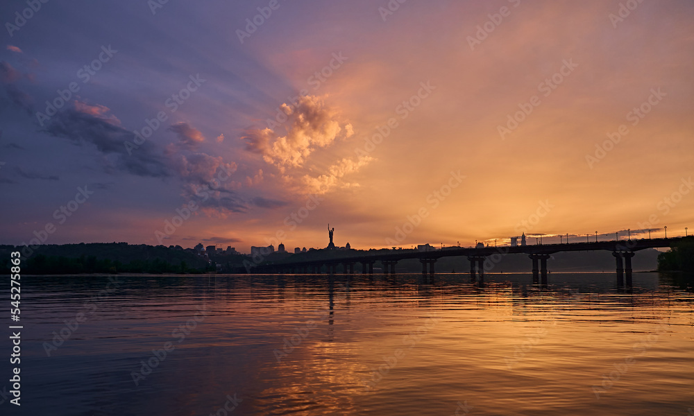 Orange blue sunset on the Dnieper river in Kyiv. Panorama of the bridge. Clouds in the sky.