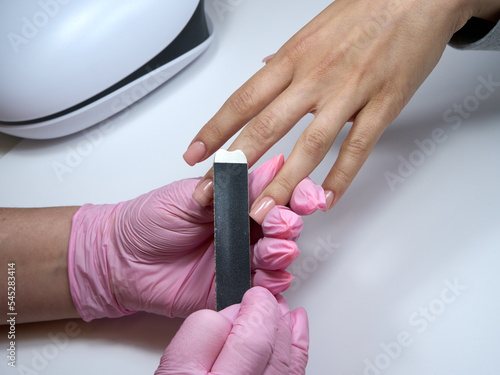 A manicurist rubs off nail polish while performing a manicure using a nail file.