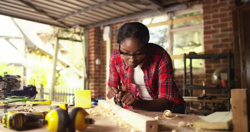 African American female carpenter wearing protective mask sanding a wooden plank with electric sander. carpentry, craftsmanship and handwork concept African American female carpenter wearing protective mask sanding a wooden plank with electric sander. carpentry, craftsmanship and handwork concept