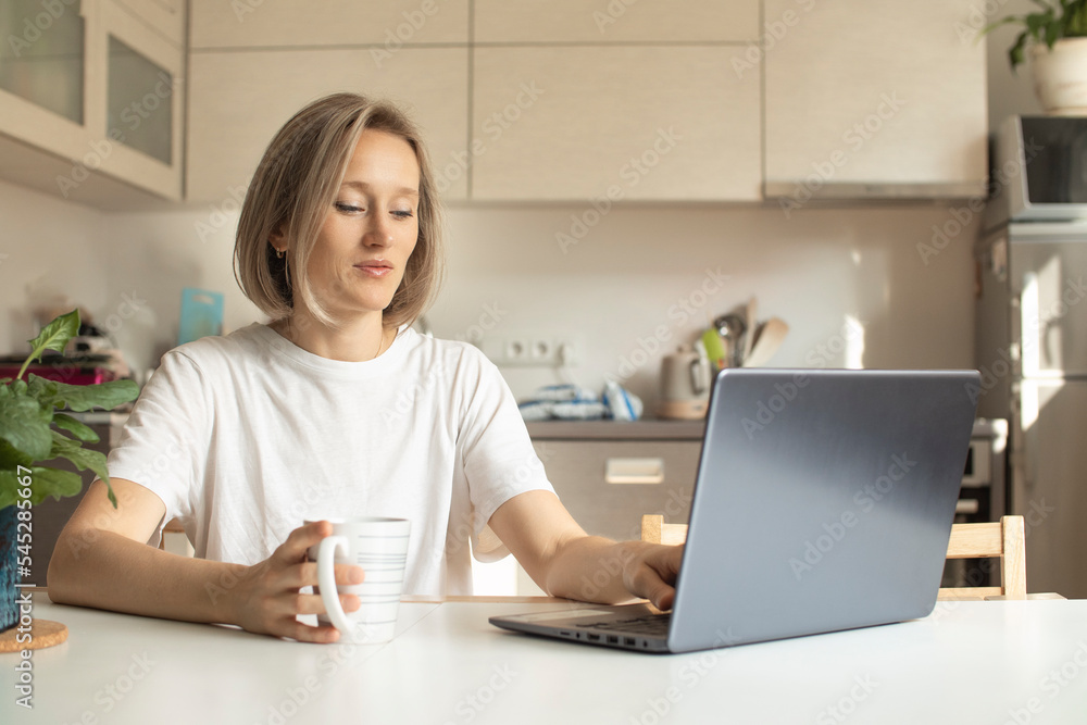woman in the kitchen with a mug and a laptop woman in the kitchen with a mug and a laptop