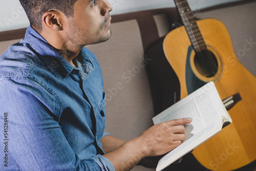 Leinwand Poster joven sentado en su sala, leyendo un libro, estudiando, guitarra y celular