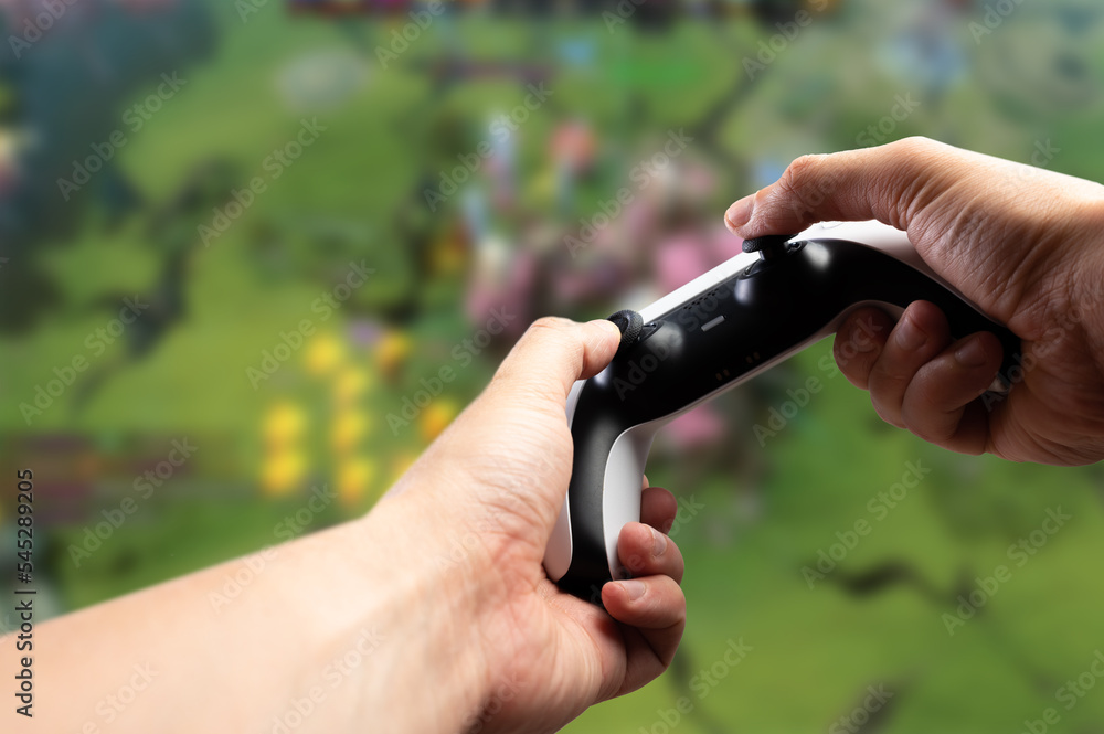 Fototapeta premium A modern gadget-joystick GAM22ICB in the hands of a gamer against the background of an exciting video game on a large TV screen, a personal computer monitor. Virtual reality.