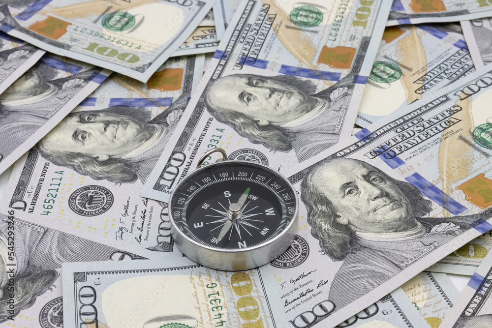Classic navigational compass on the background of one hundred dollar bills Classic navigational compass on the background of one hundred dollar bills