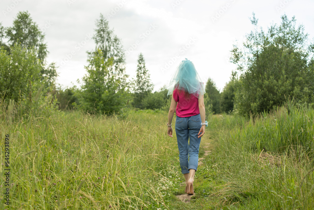 Girl walking on grass. Beautiful woman goes into distance. Jeans and veil on his head. Girl walking on grass. Beautiful woman goes into distance. Jeans and veil on his head.