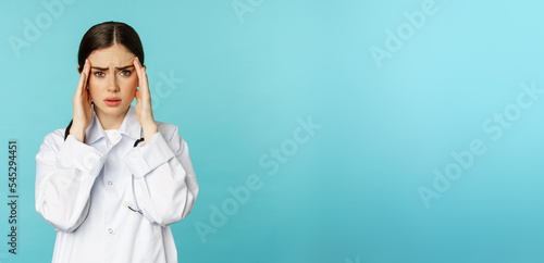 Image of woman doctor, medical personel grimacing from discomfort, having headache, migraine, feeling deezy, standing over torquoise background