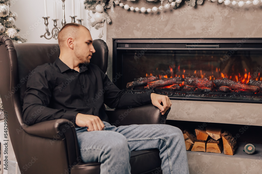 Man sitting near artificial fire electric bright fireplace with