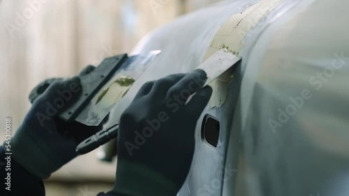 Car body repair. Mechanic apply putty on the car body with a spatula.
