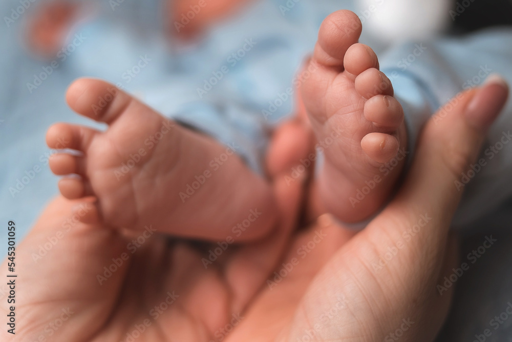 Close-up, mother's hands hold the tiny legs of newborn baby. Close-up, mother's hands hold the tiny legs of newborn baby.