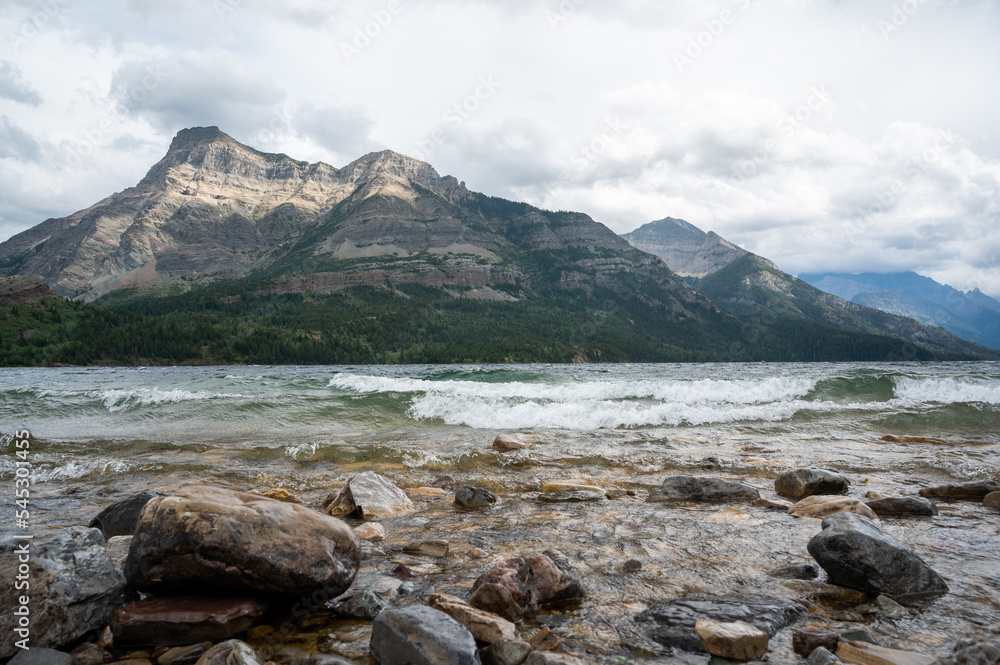 Waves crash on shore backed by mountains, Waterton Lakes National Park, Alberta. Canada