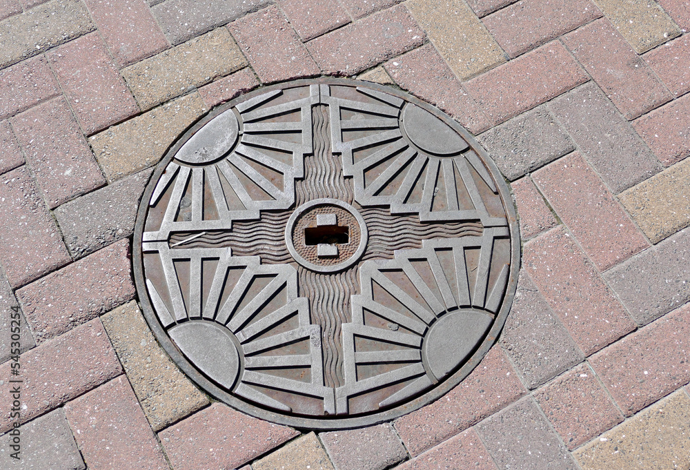 1930's art deco manhole cover in cobblestone road