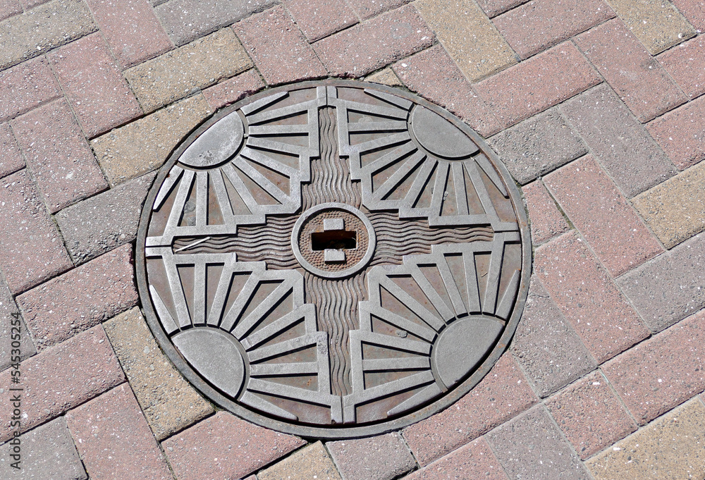 1930's art deco manhole cover in cobblestone road 1930's art deco manhole cover in cobblestone road