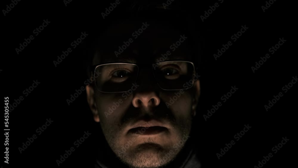 the man in glasses looking in camera on a black background in low key anger, psychopath emotions. Horror maniac face in pulsing light. Mental disorder of mind. the man in glasses looking in camera on a black background in low key anger, psychopath emotions. Horror maniac face in pulsing light. Mental disorder of mind.