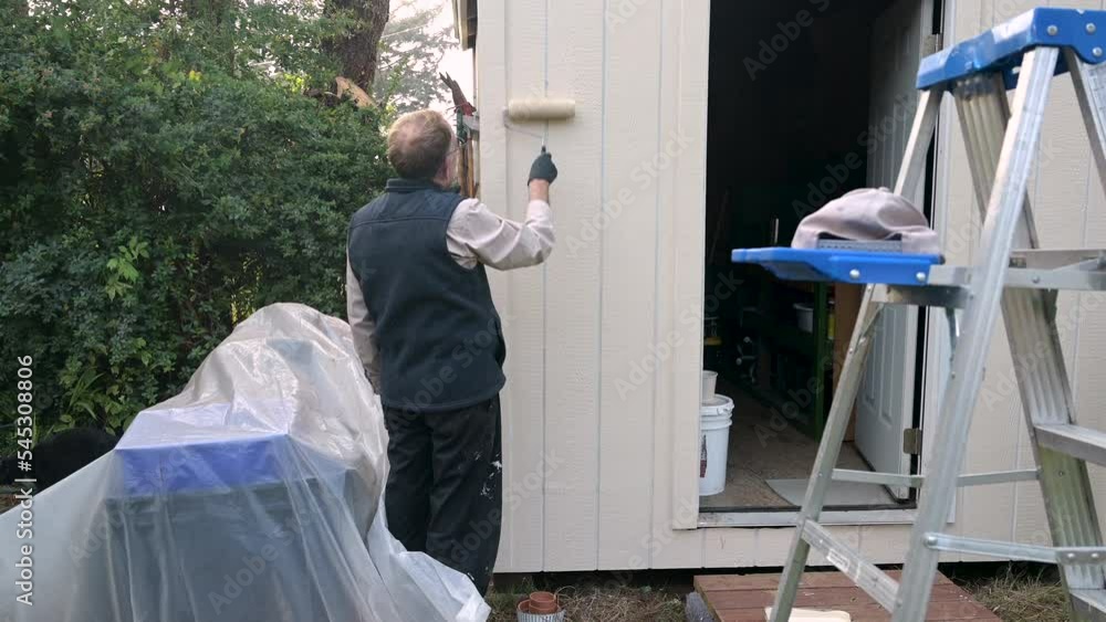 Male handyman outside paints shed with a roller. Male handyman outside paints shed with a roller.