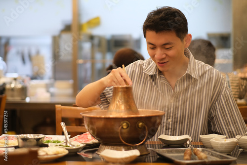 smiling Chinese young man eating Instant-boiled mutton hot pot in restaurant, a traditional Chinese hotpot photo