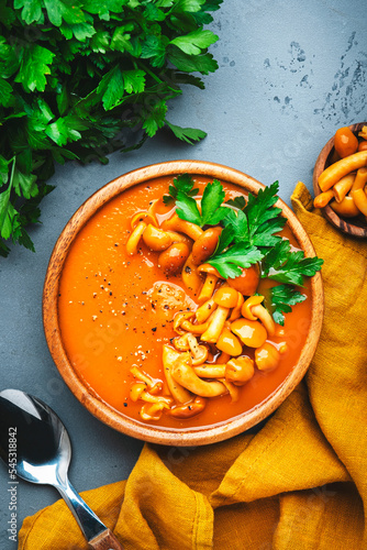Spicy pumpkin carrot soup puree with mushrooms, pepper and parsley. Winter or autumn healthy vegan vegetarian food. Soup bowl on gray table background. Top view
