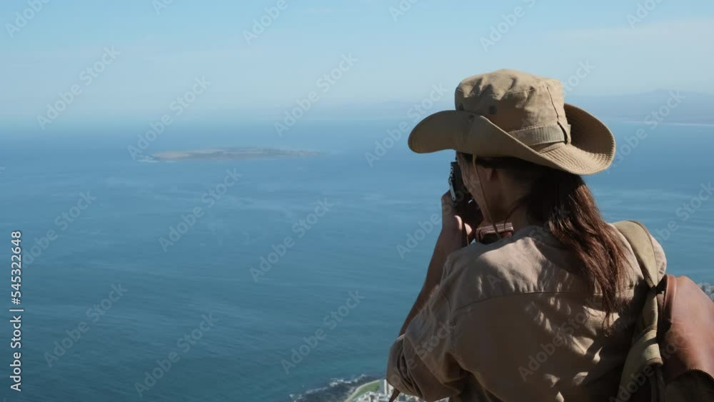 traveler in safari clothes and a hat takes a photo of the ocean from a high mountain. a hiker in boots and shorts climbed a mountain pass and takes a photo of the mountains. photographer with camera traveler in safari clothes and a hat takes a photo of the ocean from a high mountain. a hiker in boots and shorts climbed a mountain pass and takes a photo of the mountains. photographer with camera