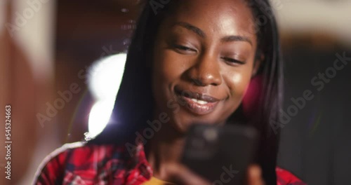 Smiling happy African American woman holding smartphone, girl checking social network news online, reading texting message on cell or using app on new mobile phone at home