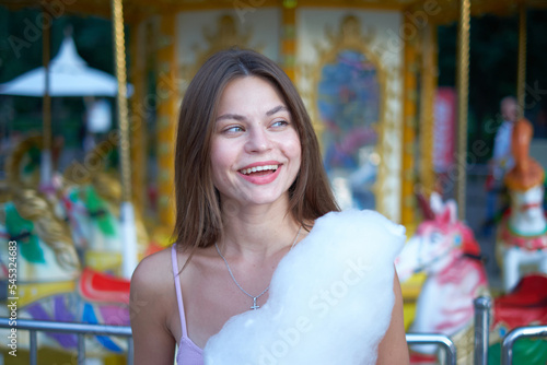 Stylish beautiful young girl walks around the amusement park, eats cotton candy and has a great time