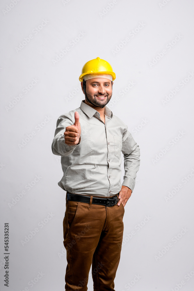 Young Indian engineer wearing yellow color hard hat and showing thumps up on white background. Young Indian engineer wearing yellow color hard hat and showing thumps up on white background.